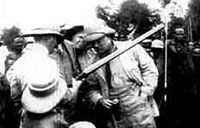 TR examines a gun before presenting it to Chief Okawahki in "TR in Africa" (1909).